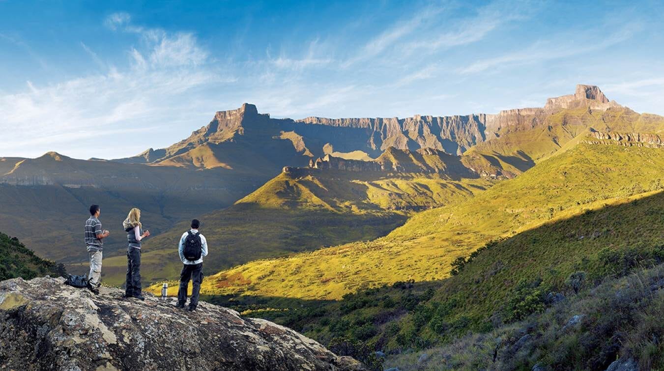 Drie wandelaars kijken vanaf een rots naar het Unesco Drakensberg Amfitheater