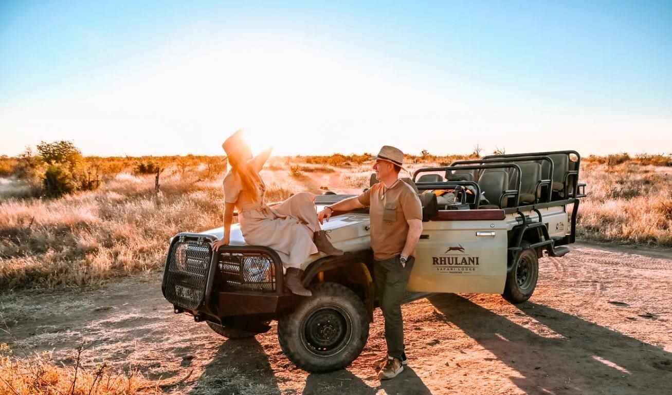 Rhulani Safari voertuig met jonge dame poserend op de moterkap en jonge man die toekijkt in Madikwe-west