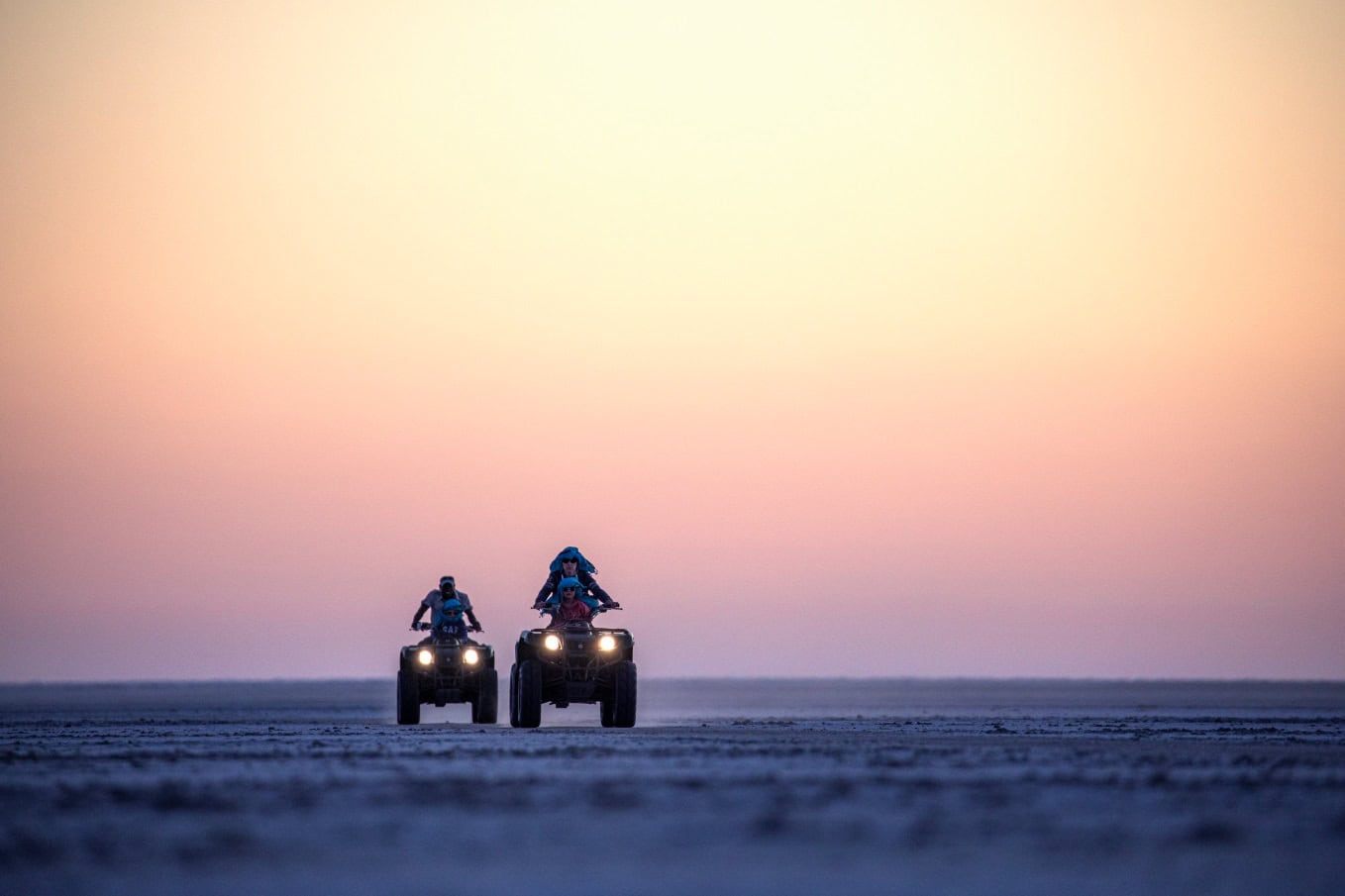 Twee quad-bikes rijdens over de Makgadikgadi zoutpannen tegen een achtergrond van violet gekleurd avondlicht
