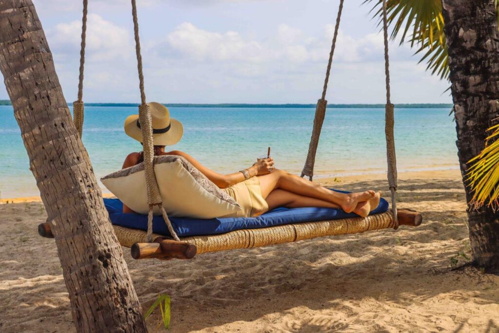 Vrouw met zonnehoed op een swingbed bij Manda Bay Lodge